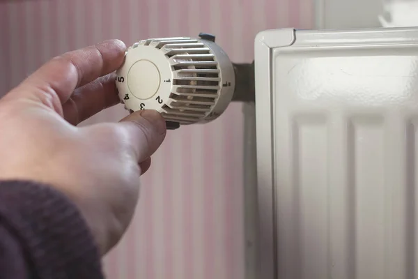 Hand turns off the radiator thermostat to a minimum with the arrival of spring and warming in the apartment against. — Stock fotografie