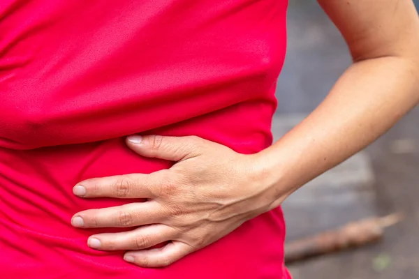 Mulher em uma camiseta vermelha tem dor abdominal intensa e cobre com a mão. Close-up. — Fotografia de Stock