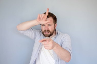 Gündelik giysiler içindeki kızgın beyaz adam ezik bir jestle birine hakaret ediyor, parmakları alnında ve işaret parmağıyla..