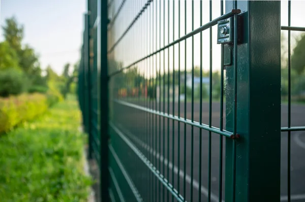 Sports ground is fenced with a green welded mesh fence, outdoors, in the evening at sunset.