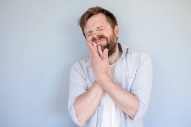 Gömlek giyen genç Avrupalı dişleri ağrıyor, yanak yanağa tutuşuyor, gözlerini kapıyor ve yüzünü buruşturuyor. Tıbbi konsept. 