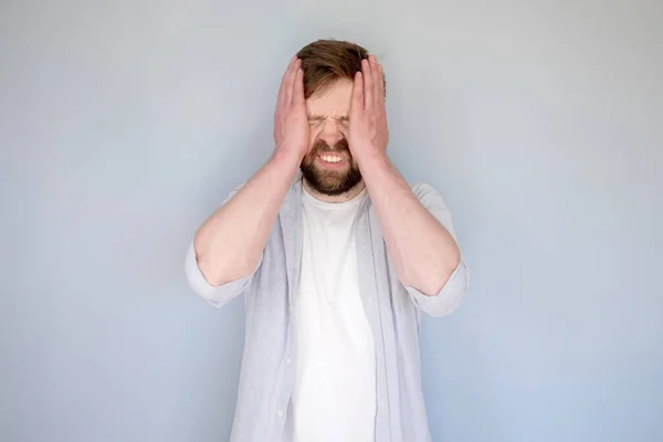 Hombre caucásico en estrés o que sufre de dolor de cabeza, cerró los ojos, sostiene la cabeza con las manos y los dientes bares. Fondo gris. — Foto de Stock