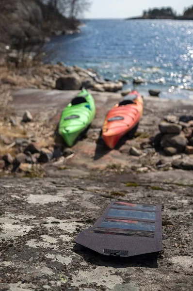 Pannelli solari portatili si trovano sulla riva pietrosa di accumulare energia, sullo sfondo dei kayak parcheggiati e bel paesaggio marino. — Foto Stock