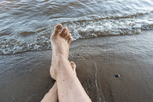 Pés femininos molhados em uma praia de areia perto da água. Mulher está descansando enquanto está sentado junto ao lago, em um dia de verão. Estilo de vida. — Fotografia de Stock
