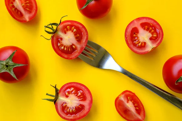Red tomatoes and a fork lie on a yellow background. Beautiful picture. Sliced and whole vegetables with cutlery, top view. — Stock Photo, Image