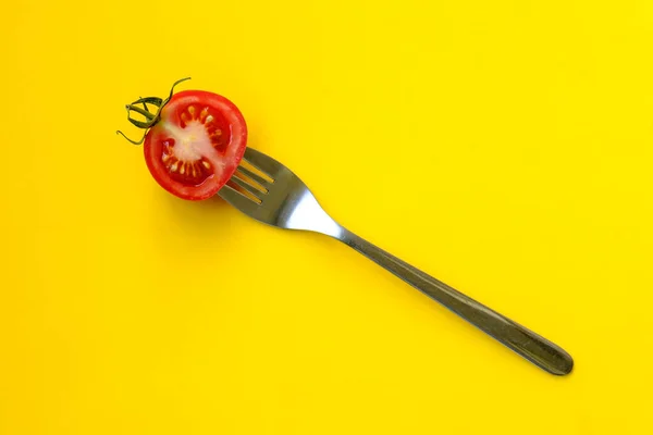 Red tomato with herbs on a fork, on a yellow background. Beautiful picture. Ripe, sliced vegetable with cutlery isolated in the studio. Top view. — Stock Photo, Image