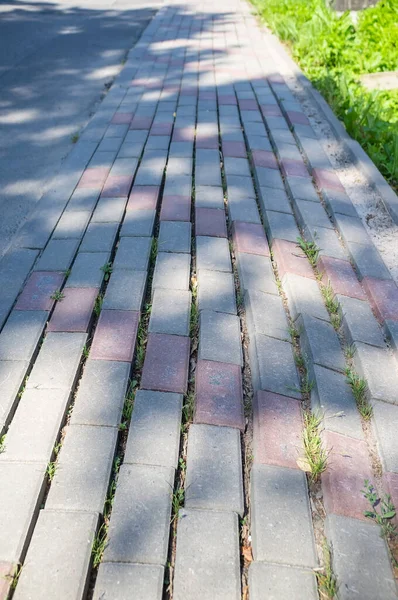 Pavimento pavimentado con piedra, con defecto. Camino peatonal mal hecho, en la ciudad, en un día de verano. — Foto de Stock