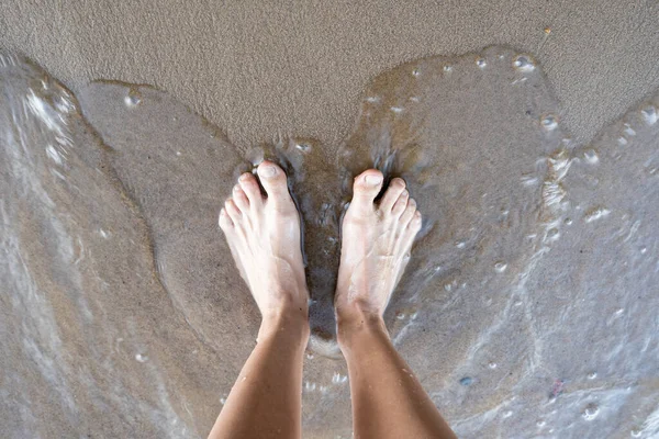 Las mujeres bronceadas piernas están en el agua, en la orilla arenosa del río, en un día de verano. Estilo de vida. Vista superior. —  Fotos de Stock