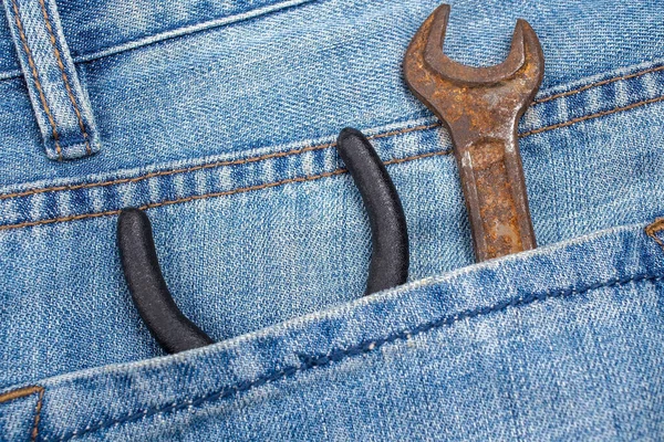 Chiave arrugginita e pinze sono nella tasca posteriore dei jeans. Attrezzo in abiti da lavoro speciali. Primo piano. — Foto Stock
