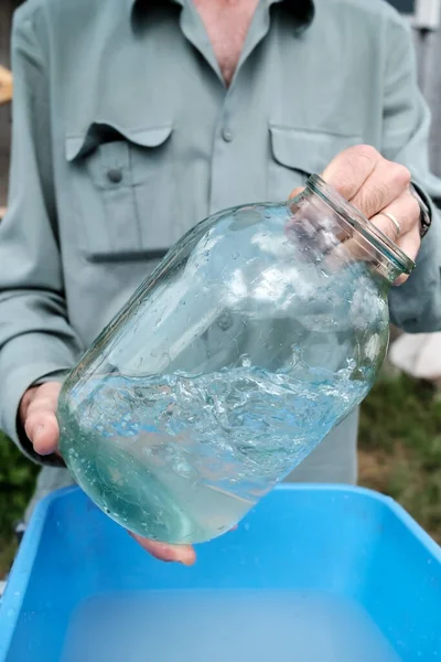 Ein Mann wäscht an einem Sommertag ein schmutziges Glasgefäß in einem Plastikbecken auf einem Dorfplatz. Ländliche Traditionen. — Stockfoto