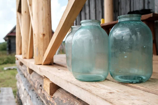 Грязные стеклянные банки стоят на деревянном крыльце деревенского дома, во дворе. — стоковое фото
