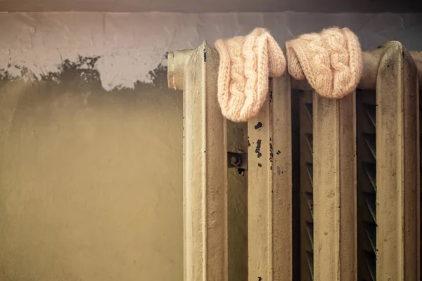 Les mitaines humides tricotées séchent sur un vieux radiateur chaud après une promenade hivernale, sur le fond d'un mur. — Photo