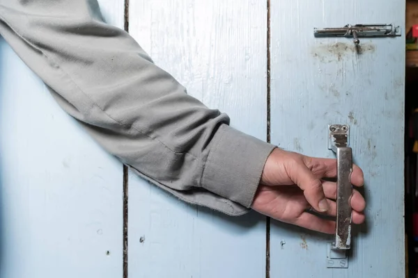 Mann in Hemd öffnet eine Holztür mit einem in blau lackierten Riegel in einem Dorfhaus. — Stockfoto