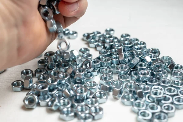 Mano de un mecánico masculino esparciendo tornillo nuevo y brillante como joyas en una mesa blanca. — Foto de Stock