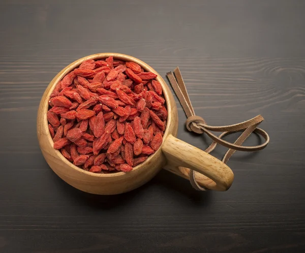 Bacche di Goji in una ciotola di legno, che si trova su un tavolo nero — Foto Stock