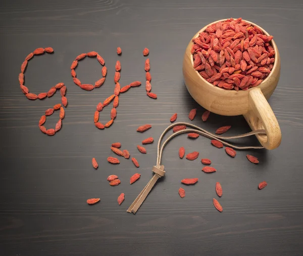 Caption goji berries on a black table, next to a cup filled — Stock Photo, Image