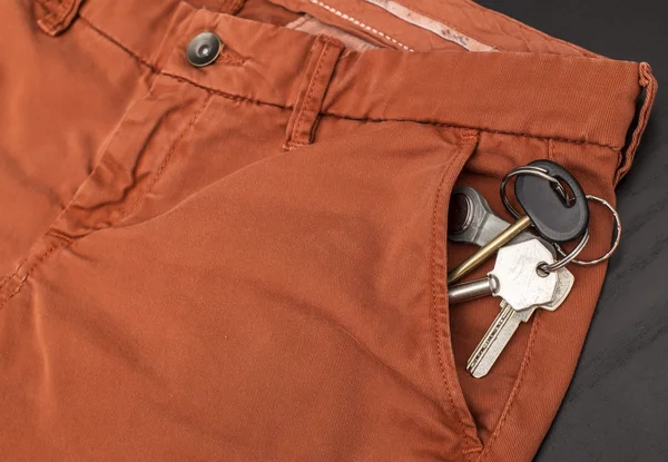 Куча ключей торчит из кармана брюк, которые лежат на столе. — стоковое фото