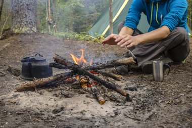 Kamp sırasında oturan kız ısıtmalı yangın yakın ve sıcak çay içmek