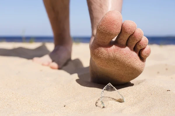 Uomo va sulla spiaggia e il rischio di calpestare una scheggia di vetro bottiglia rotto — Foto Stock