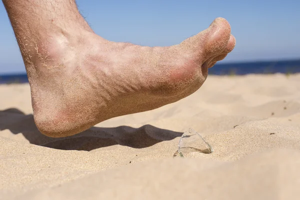 Uomo va sulla spiaggia e il rischio di calpestare una scheggia di vetro bottiglia rotto — Foto Stock