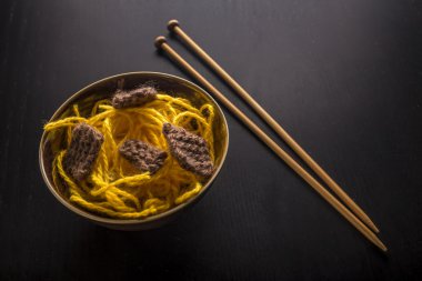 Food knitted from woolen thread lies on a plate, as a Japanese dish of meat and noodles, lie next to the wooden spokes, like sticks.