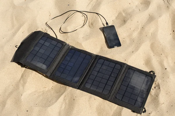 Портативная солнечная панель на пляже заряжает мобильный телефон . Стоковое Изображение