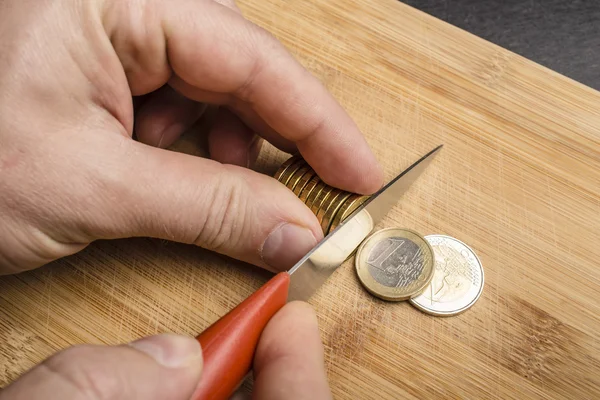 Handgeschnittene Euromünzen mit einem Messer auf einem Schneidebrett — Stockfoto