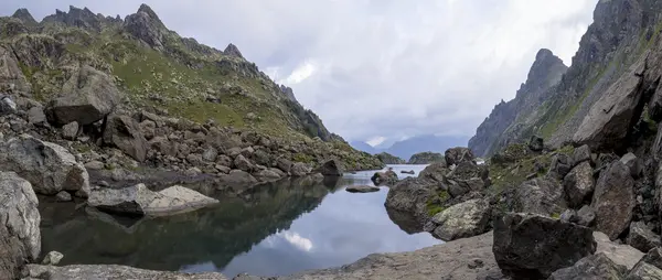 Panoramalandschaft mit einem See in den Bergen, riesigen Felsen und Steinen an der Küste und dem Widerschein von Wolken — Stockfoto