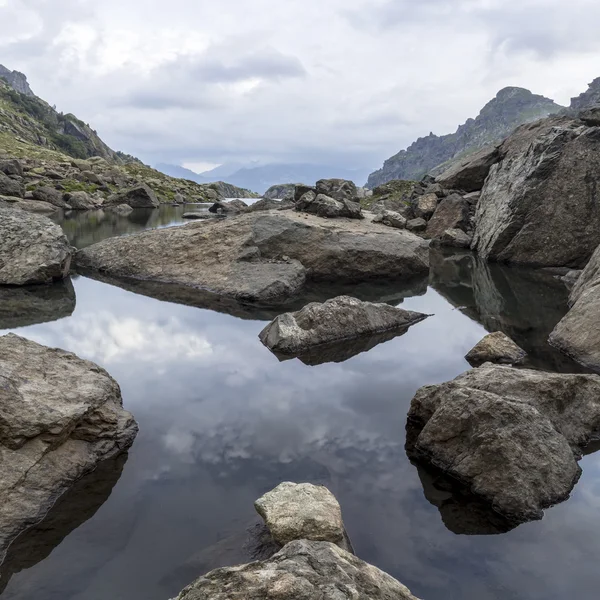 Panoramalandschaft mit einem See in den Bergen, riesigen Felsen und Steinen an der Küste und dem Widerschein von Wolken — Stockfoto