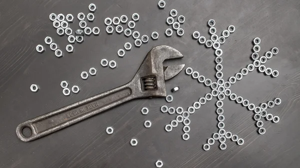 Sign snowflake made up of screws nuts on a dark wooden table — Stock Photo, Image