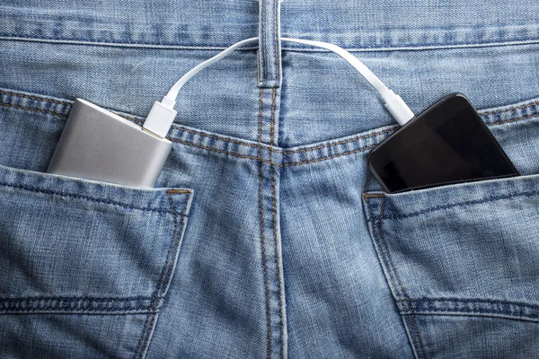 Power bank ligger i en bakficka jeans mobiltelefon sköter — Stockfoto