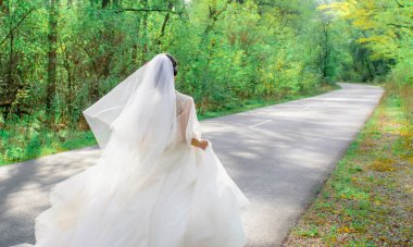 Gelin yol boyunca koşar. Rüzgarda dalgalanan beyaz gelinlik. Güneşli bir günde ağaçlarda yeşil yapraklar