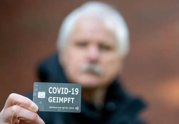 Senior man showing a German vaccination certificate, which indicates a vaccination against covid-19.