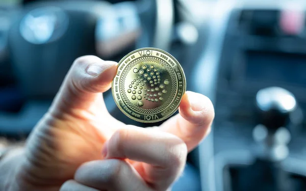 Symbol for autonomous driving. Hand holds a IOTA coin in a self driving car.