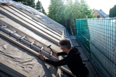 Roofer eski bir evin çatısında yeni yalıtım malzemesi tamir ediyor..