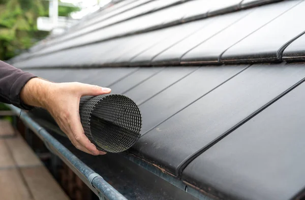 Man puts a gutter mesh to the rain gutter to protect the gutter from leaves.