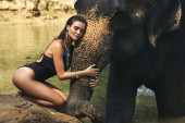 Happy young woman is bathing with the elephant in the river