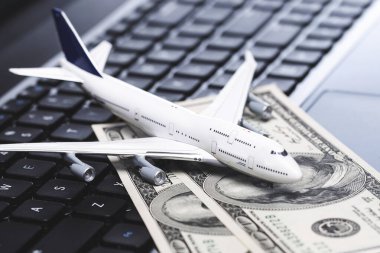 İnternetten bilet al. Küçük oyuncak uçak ve USD banknotlar dizüstü bilgisayarın üzerinde