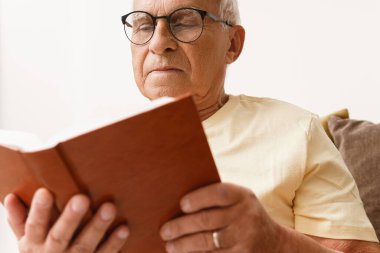 Bilge yaşlı adam evde kitap okuyor.