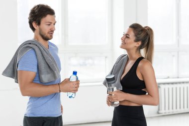 Erkek ve kadın spor salonunda iyi bir idmandan sonra konuşuyor. Birkaç şişe su ve havlu tutan çift eğitim sürecini tartışıyor..