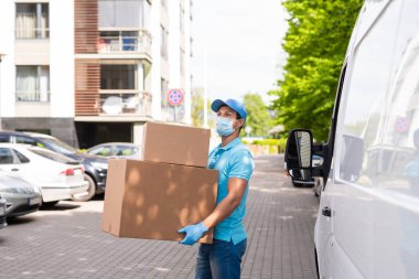 Önleme maskesi ve eldiven takan teslimatçı karton kutuları minibüsünün yanında tutuyor.