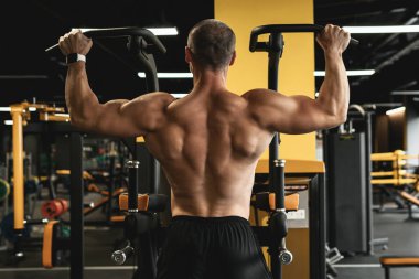 Spor salonunda egzersiz yaparken barfiks çeken kaslı vücut geliştirici.