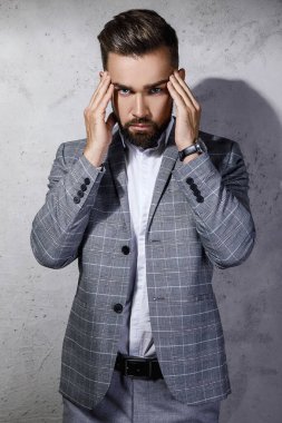 Gri kareli takım giyen yakışıklı sakallı adam beton duvara karşı poz veriyor.