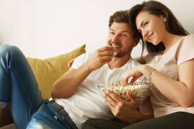 Genç ve mutlu çift evde patlamış mısır yiyip film izliyor.