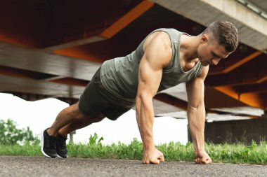Young and muscular man is doing push-ups during calisthenic workout on a street clipart
