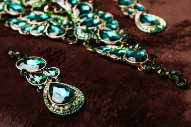 Lüks kolye ve kahverengi kadife arka planda yeşil değerli taşlar olan küpeler.