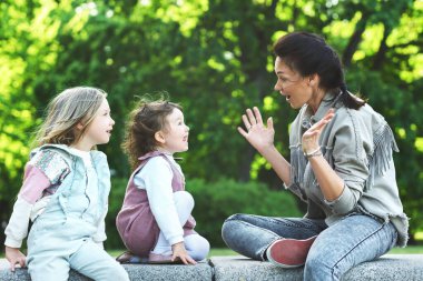 Genç mutlu anne ve iki kızı bir şehir parkında oturuyor ve oynuyorlar.
