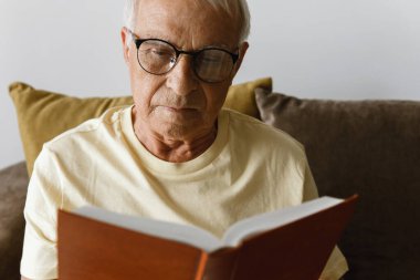 Bilge yaşlı adam evde kitap okuyor.