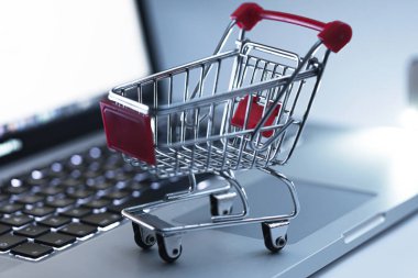 Dizüstü bilgisayarın klavyesinde minyatür alışveriş arabası. Online alışveriş ve e-ticaret kavramı.