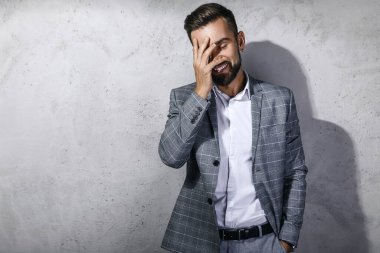 Gri kareli takım giyen yakışıklı sakallı adam beton duvara karşı poz veriyor.